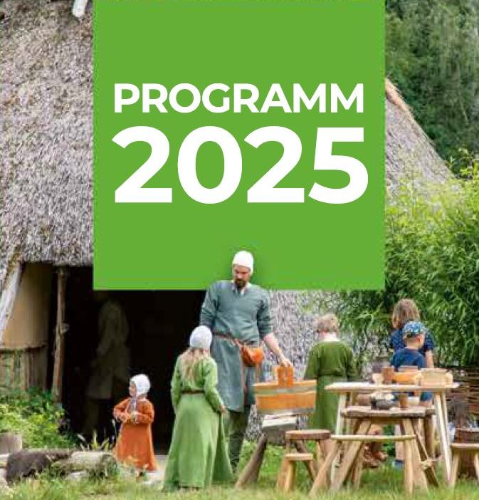 Mittelalterlich gekleidete Familie vor reetgedecktem Bauernhaus mit Kasten "Programm 2025"