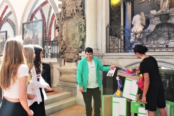 Zwei m&auml;nnliche Jugendliche pr&auml;sentieren drei weiblichen Jugendlichen eine Installation aus Kartons und Spielzeug in der Nikolaikirche